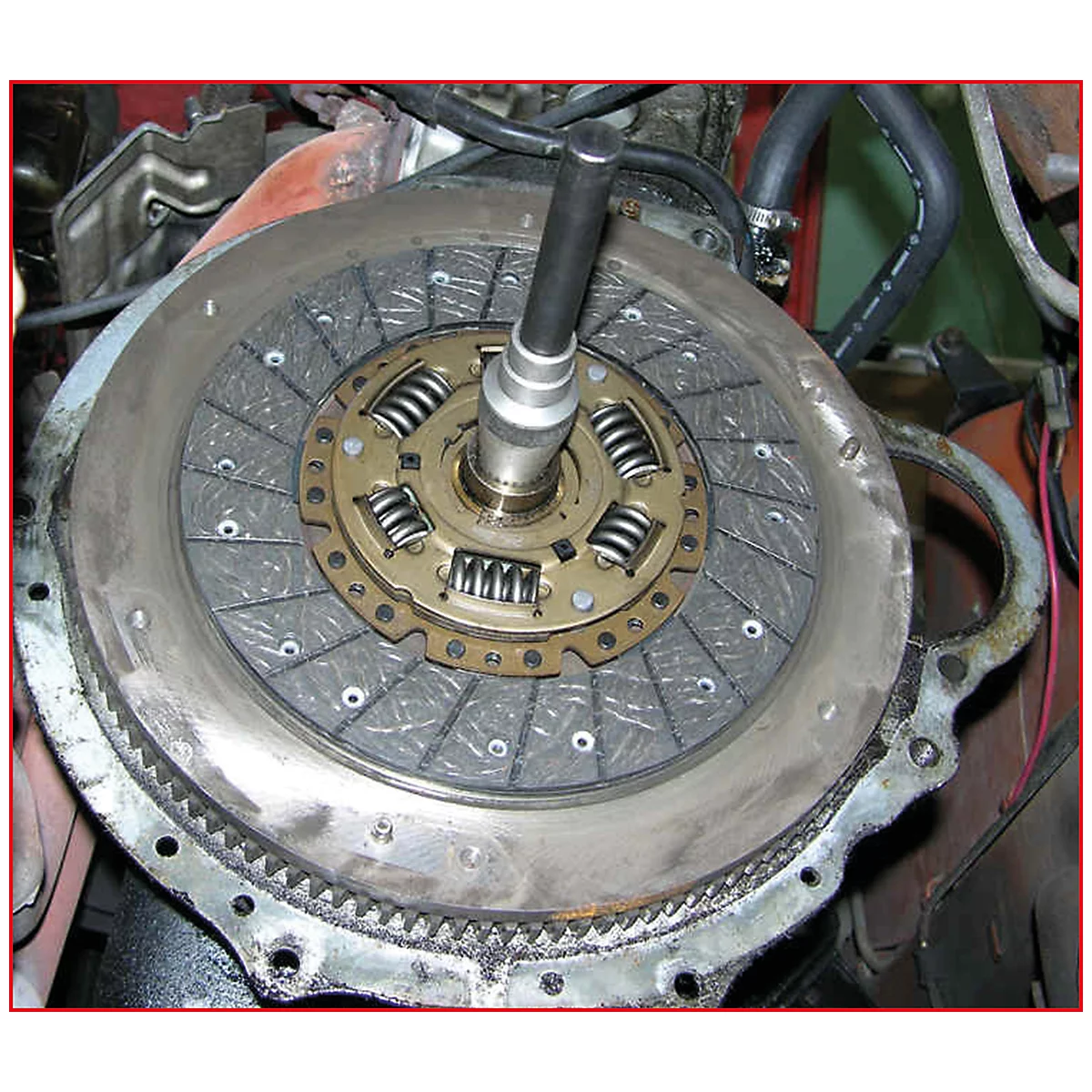 Nahaufnahme einer Kupplungsscheibe mit Werkzeug. Die Scheibe ist grau, mit metallischen Federn und einem Führungsstift.