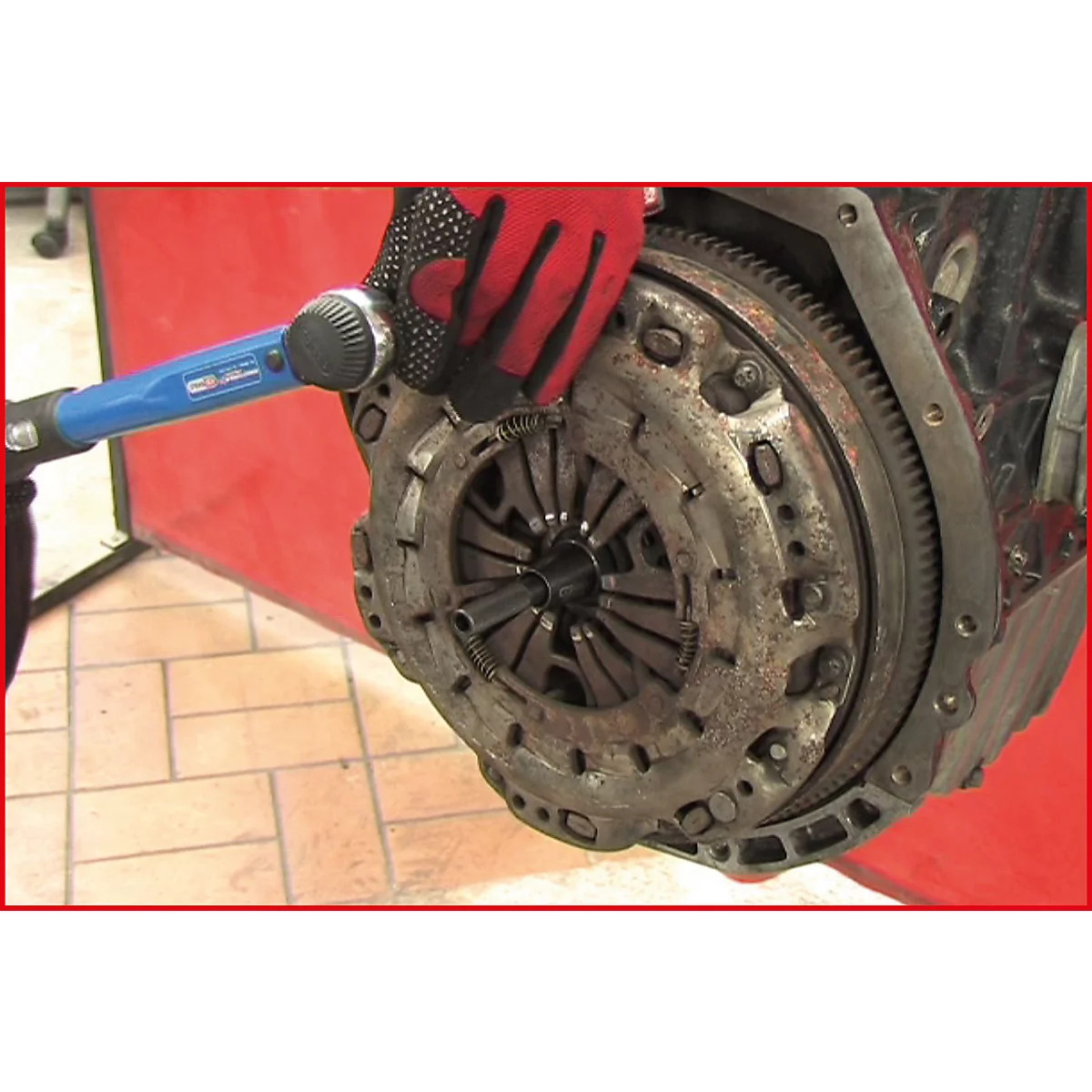 Eine Hand mit rotem Handschuh montiert mit einem blauen Werkzeug eine Kupplung an einem Motor.