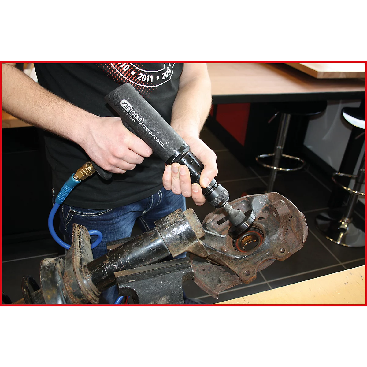 Eine Person benutzt einen Druckluftschrauber, um an einem Radaufhängungsteil zu arbeiten.