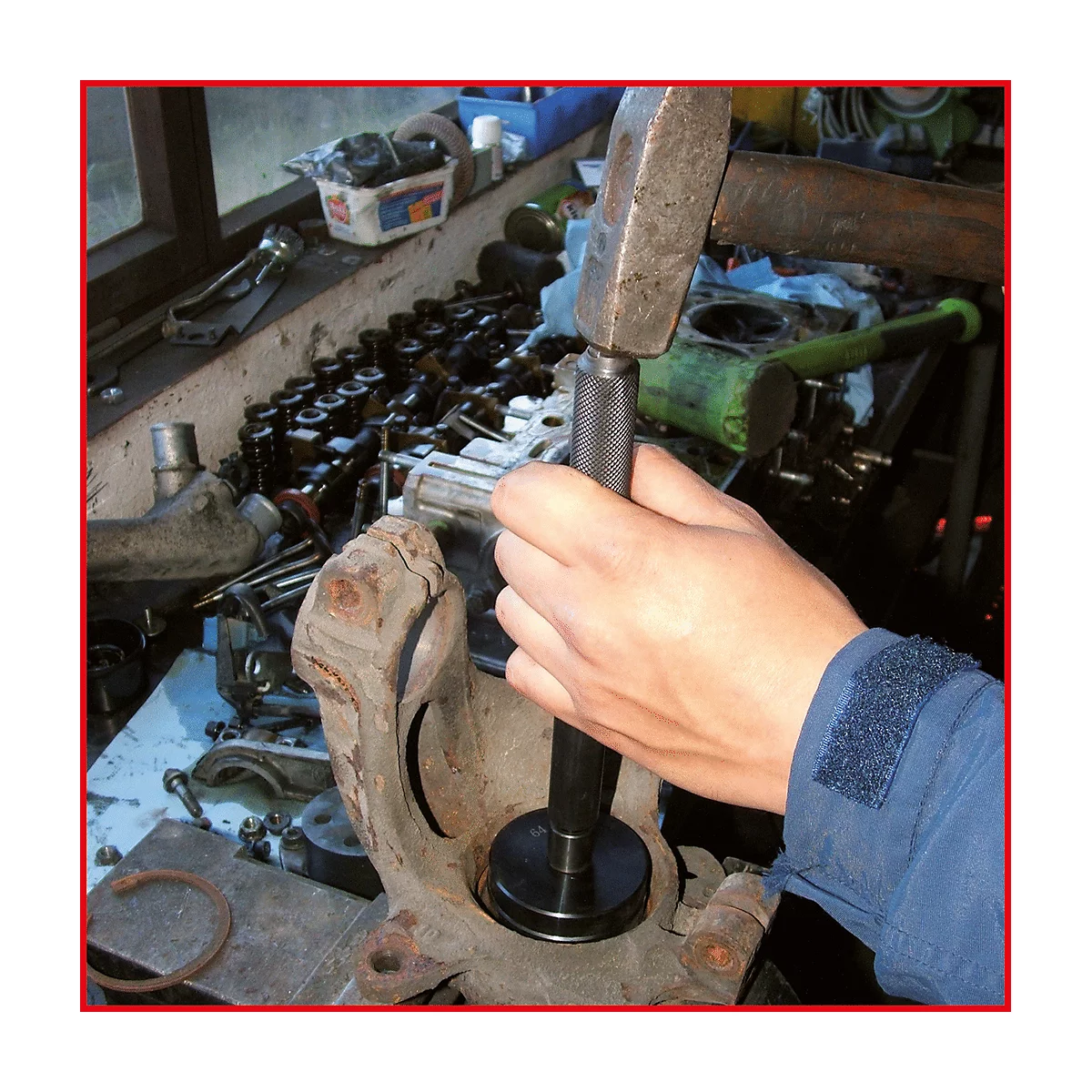 Hand mit Hammer schlägt auf Werkzeug. Werkzeug wird in ein Autoteil geschlagen.