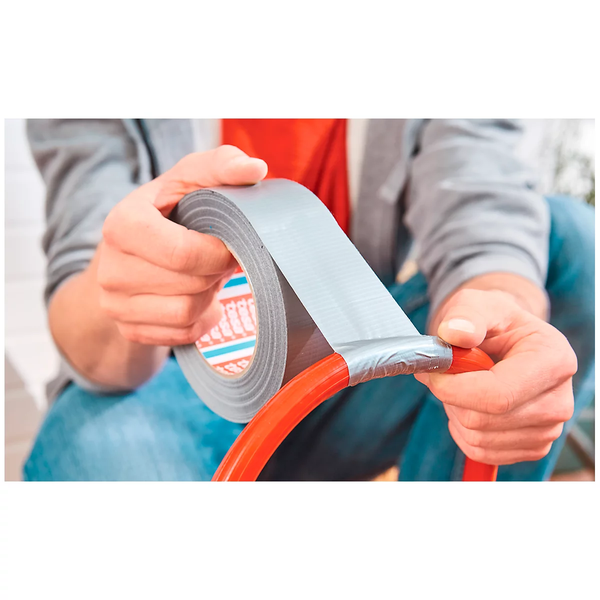 A person taping a red hose with grey duct tape. The tape has the imprint 'tesa'.