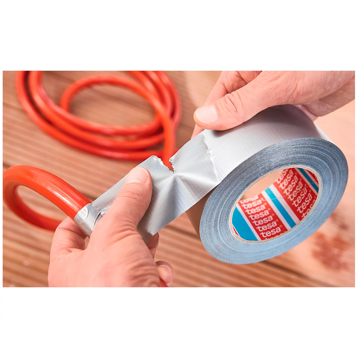 Hands taping red cable with grey tape. Tape roll with "tesa" print.