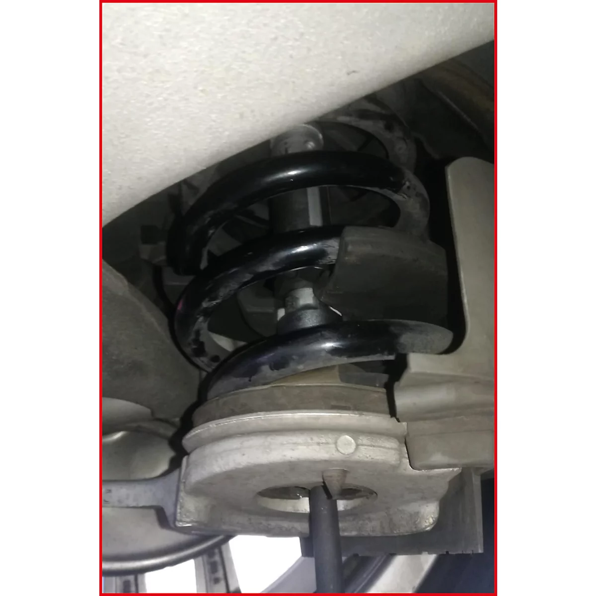 Nahaufnahme einer schwarzen Schraubenfeder in einem Fahrzeug, darunter ein metallischer Teil.