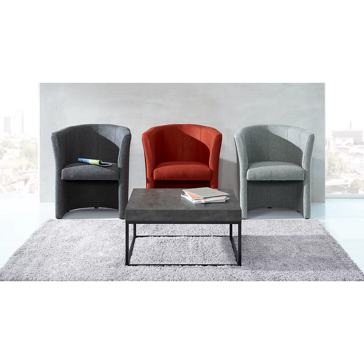 Three armchairs in gray and red in front of a wall. A gray coffee table with books sits on a gray rug.