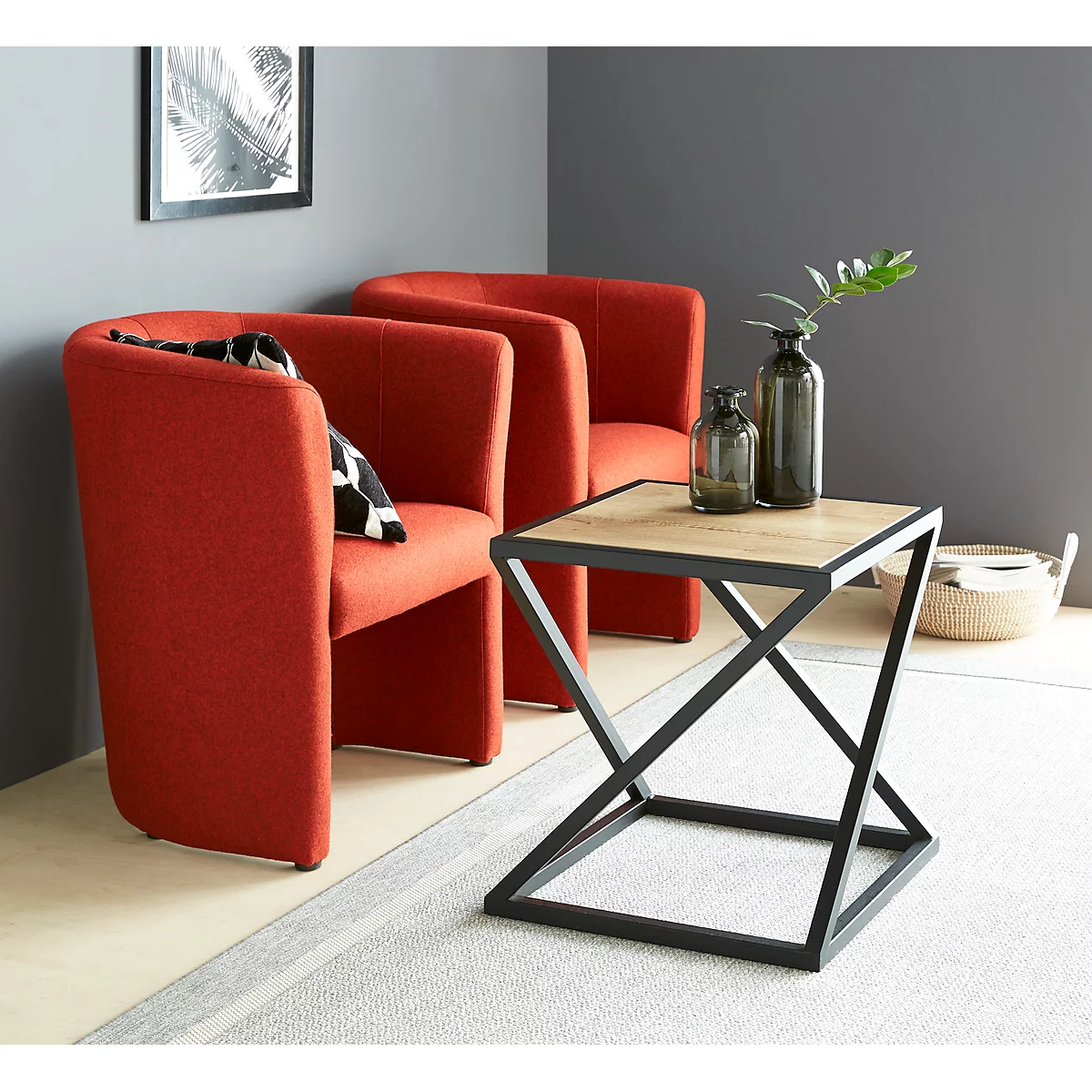 Red armchairs, side table with two vases, picture on the wall. There is a plant on the table.