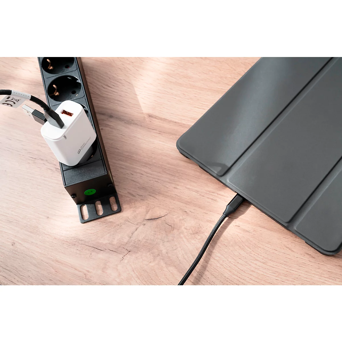 A black power strip with a white charger plugged in. A black cable connects to a gray tablet.
