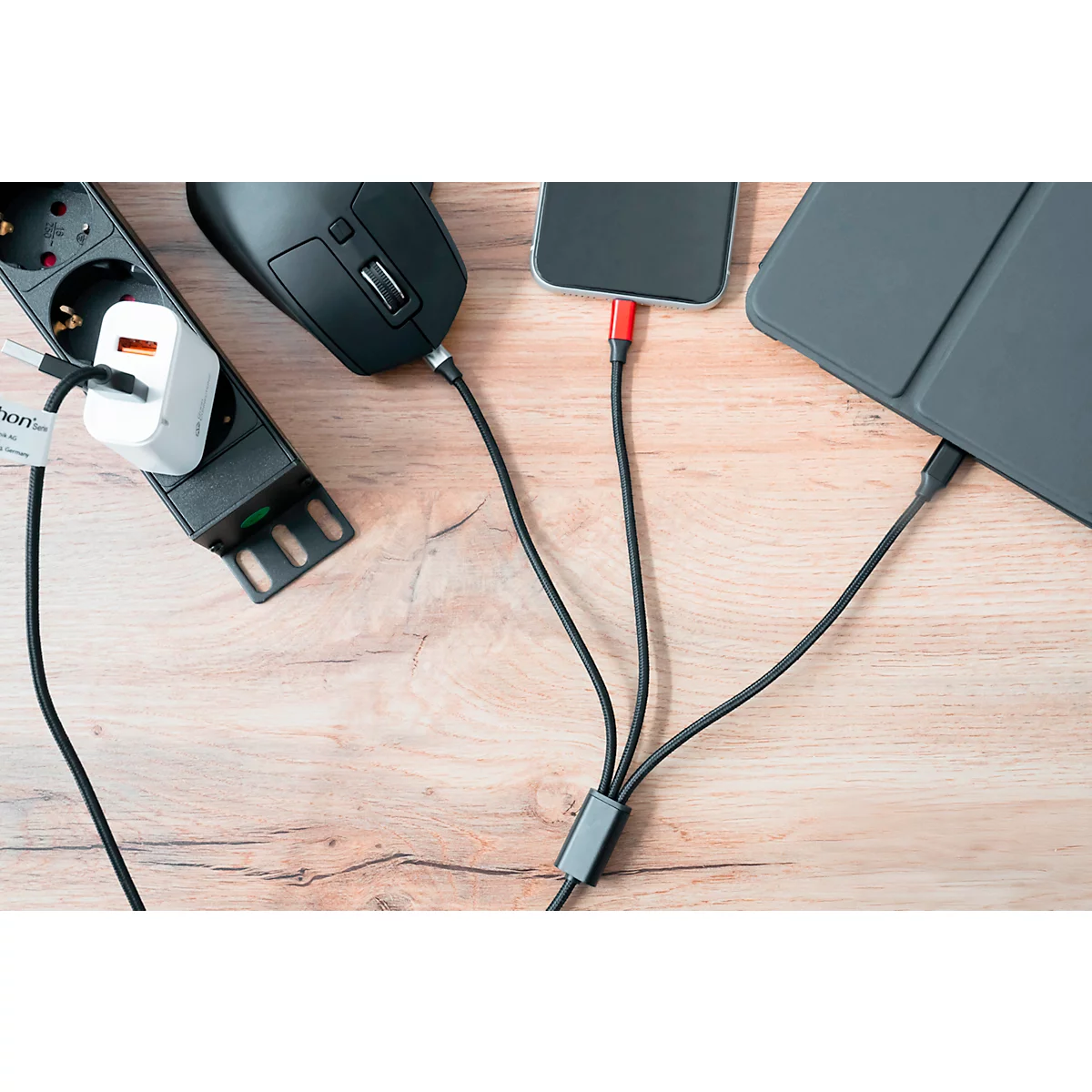 On a wooden surface, there is a power adapter, a mouse, a smartphone, and a tablet. All devices are connected via cables.