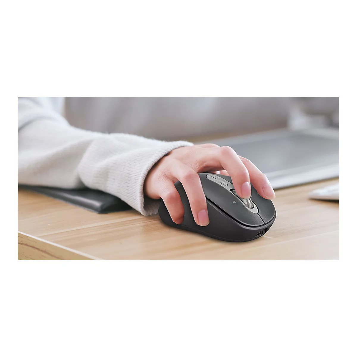 Person bedient eine schwarze Maus auf einem Schreibtisch. Die Hand ruht auf einem Handgelenkspad.