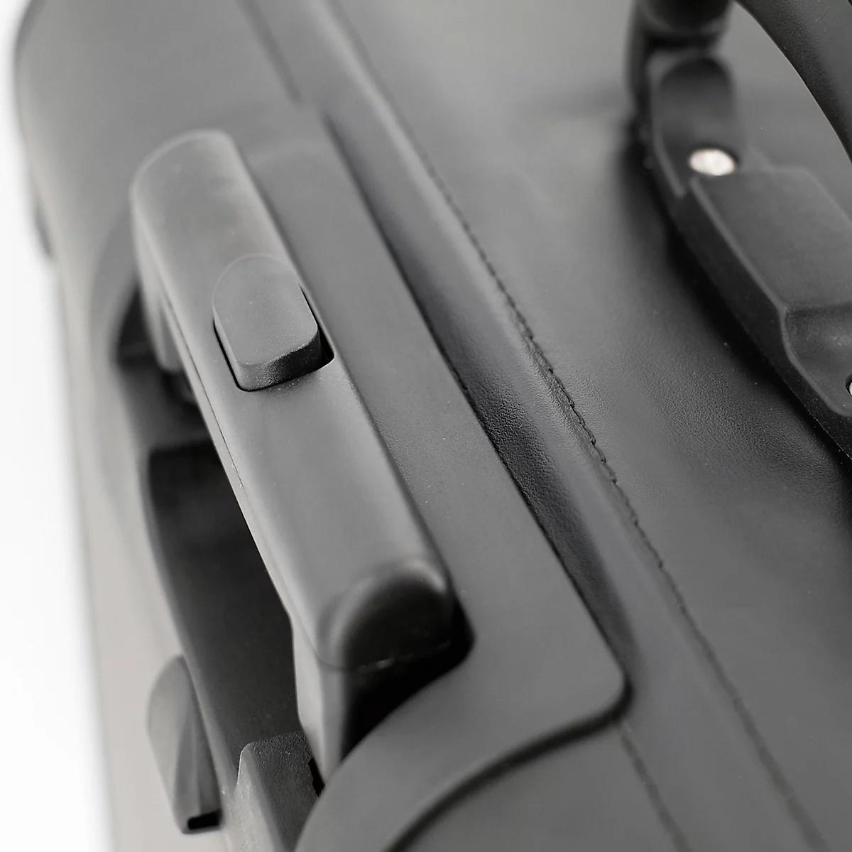 Gros plan sur une valise noire. Poignées en plastique, surface semblable au cuir. La couture est visible.