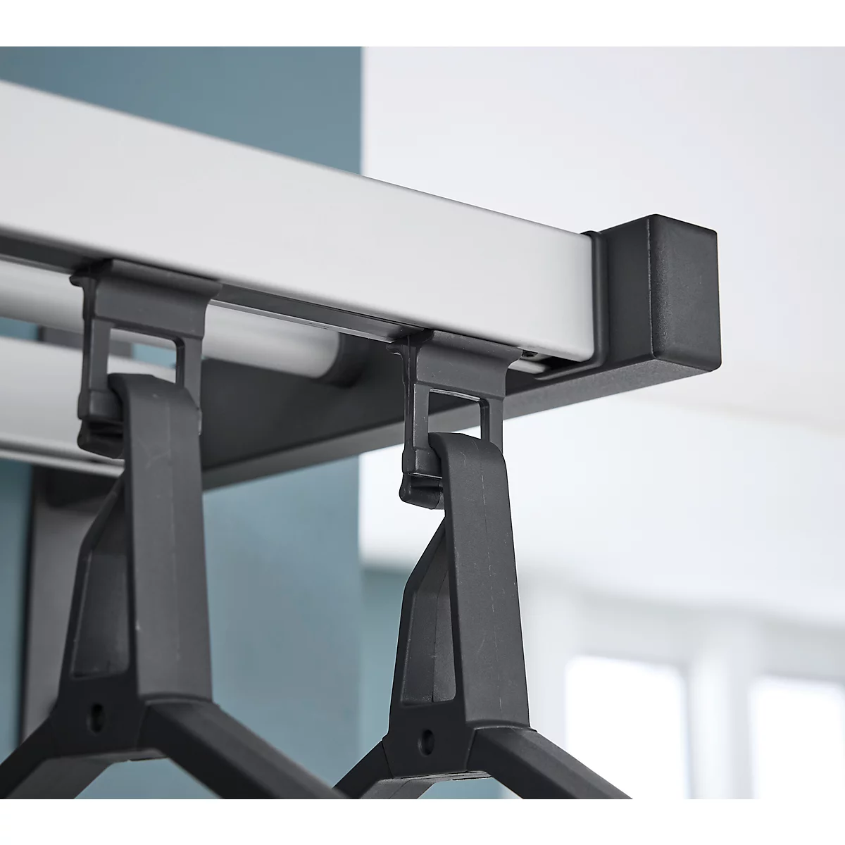 Close-up: Zwarte kleerhangers hangen aan een rail. De rail is zilverkleurig, met zwarte beugels.