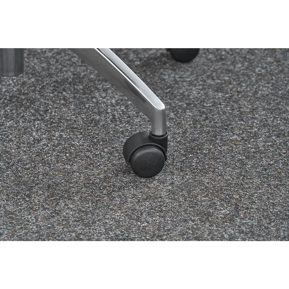 Close-up of a chair wheel and leg. The wheel is black, the leg silver. The floor is gray mottled.