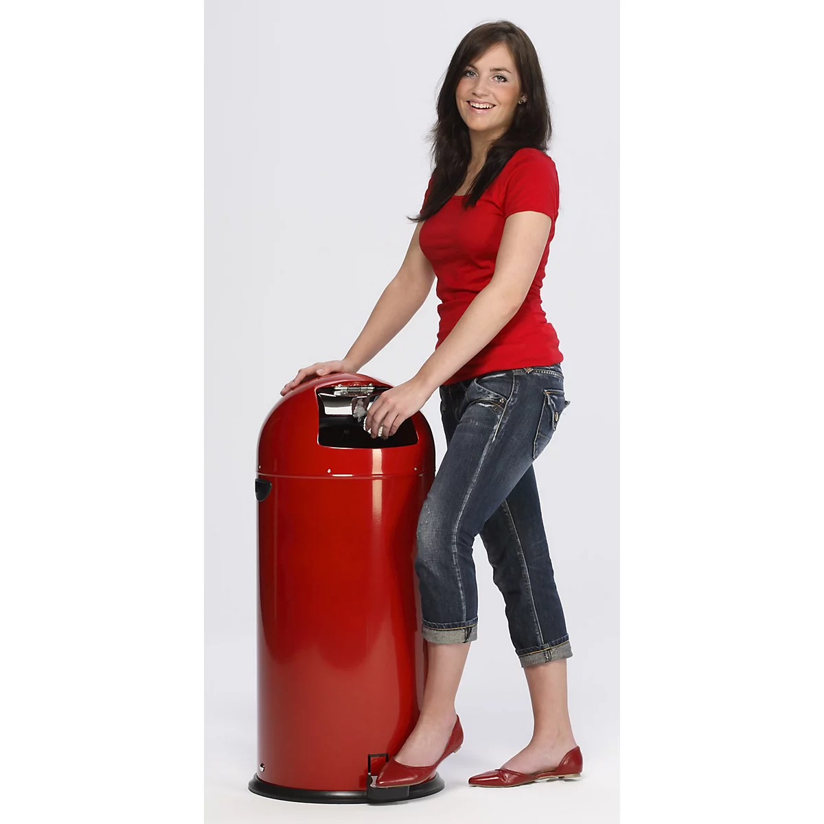Eine lächelnde Frau steht neben einem roten Mülleimer, sie drückt mit dem Fuß auf das Pedal.