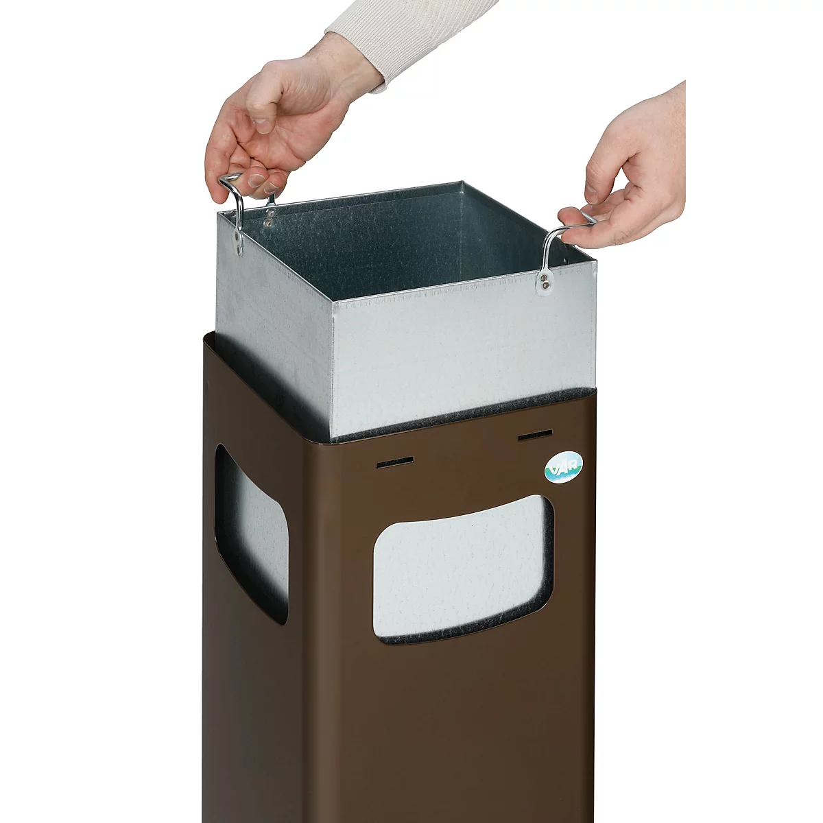 Hände heben einen silbernen Mülleimer aus einem braunen Abfalleimer.