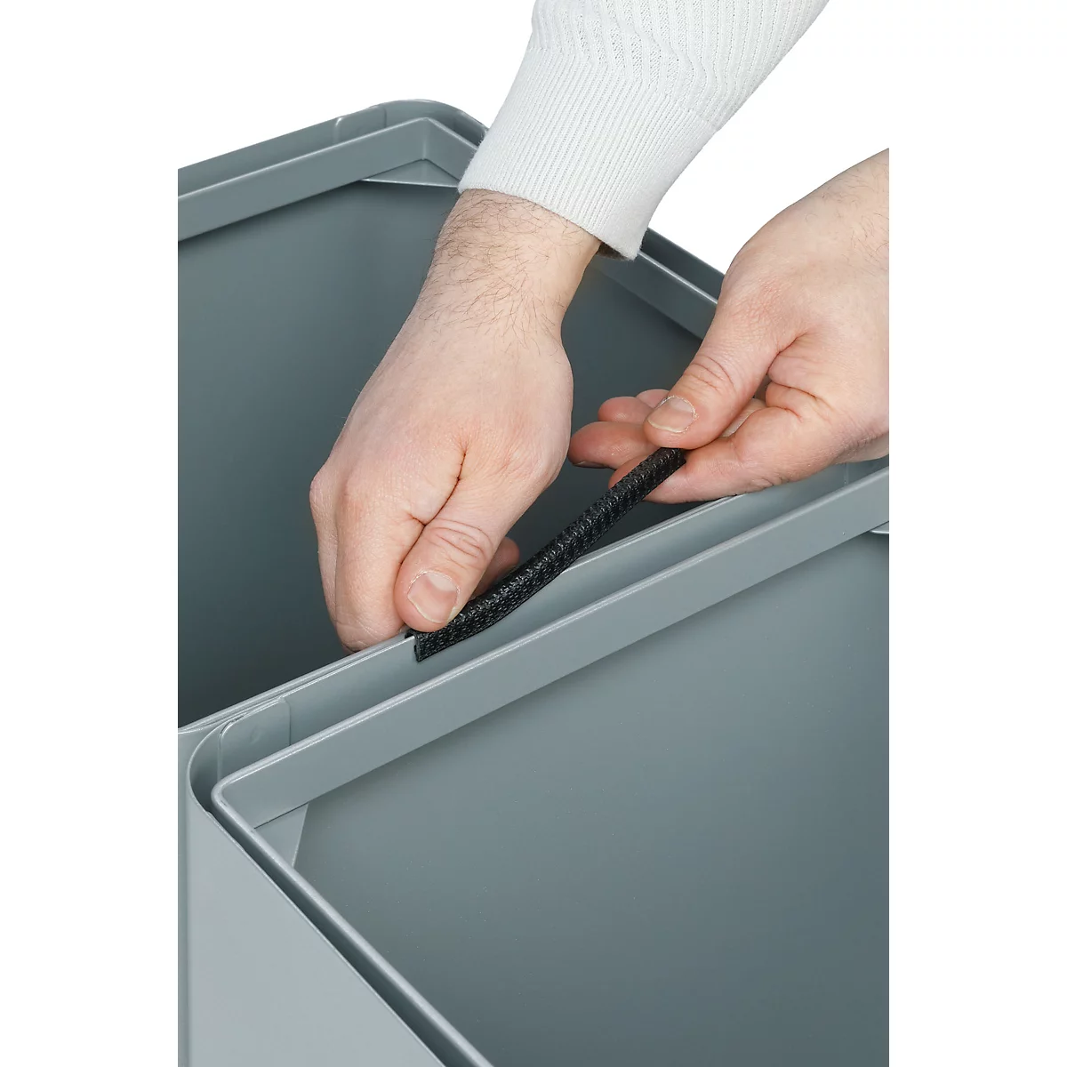 Hände halten schwarzen Gummi an grauen Mülleimer. Detailaufnahme.