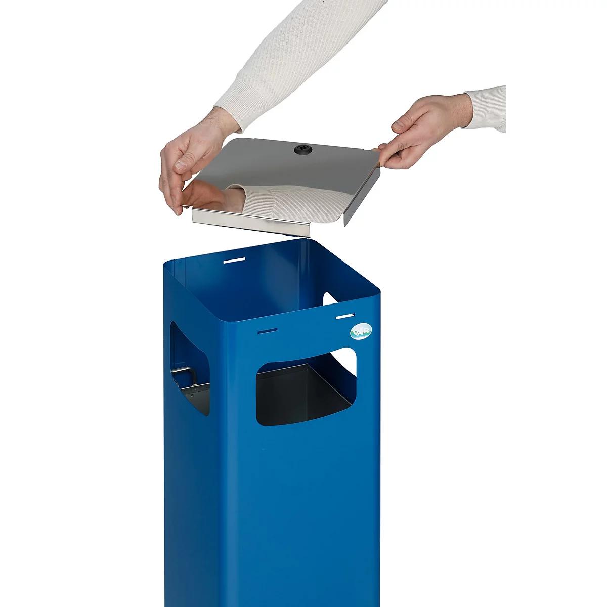 Een persoon plaatst een deksel op een blauwe vuilnisbak. Het deksel is van metaal.