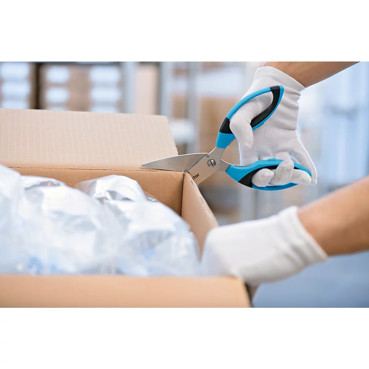 Handen in witte handschoenen snijden karton met blauwe schaar. Binnen: plastic verpakking.