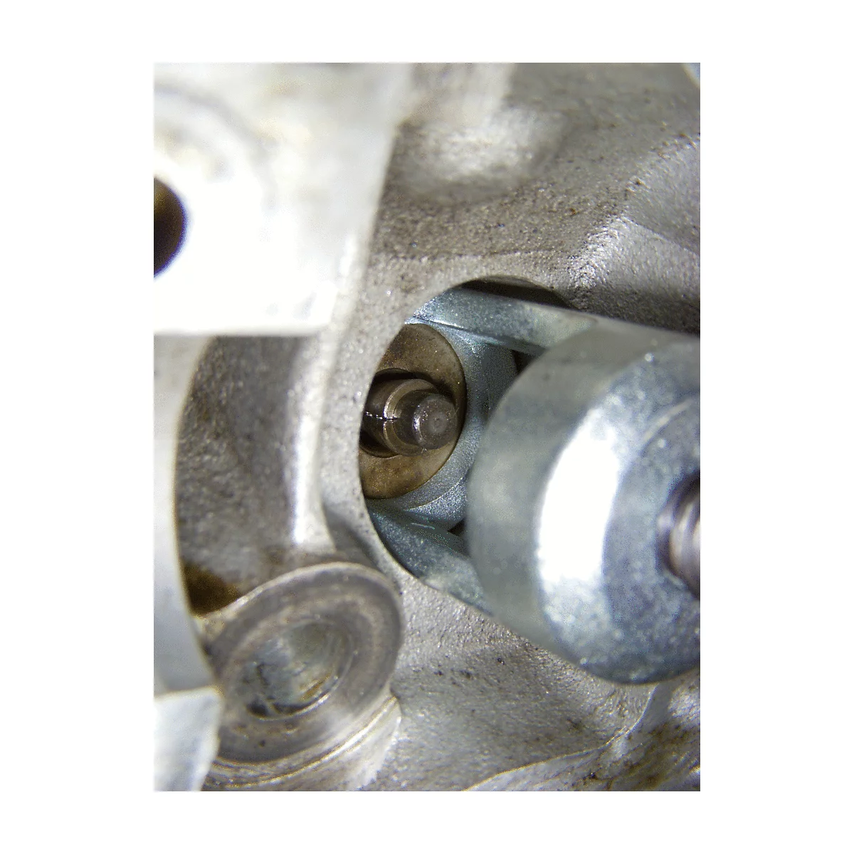 Nahaufnahme eines Motorenteils: Ein Bolzen in einer Aussparung, umgeben von grauem Metall. Ein Schraubenschlüssel liegt rechts.