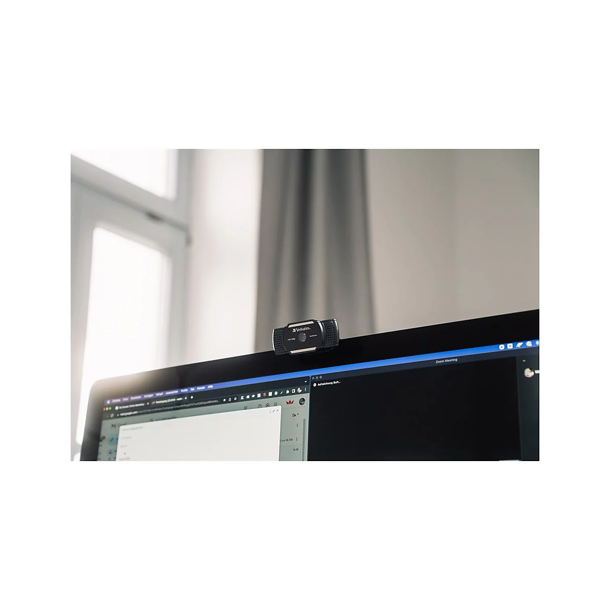 Schwarze Webcam auf einem Monitor. Im Hintergrund sind ein Fenster und VorhÃ¤nge zu sehen.