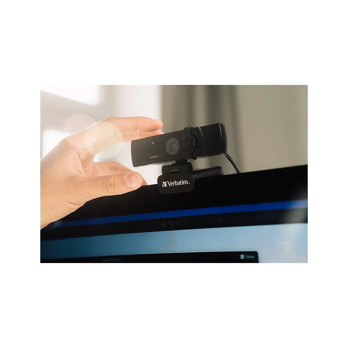 Nahaufnahme einer schwarzen Webcam, die an einem Monitor befestigt ist. Eine Hand berÃ¼hrt die Kamera sanft.