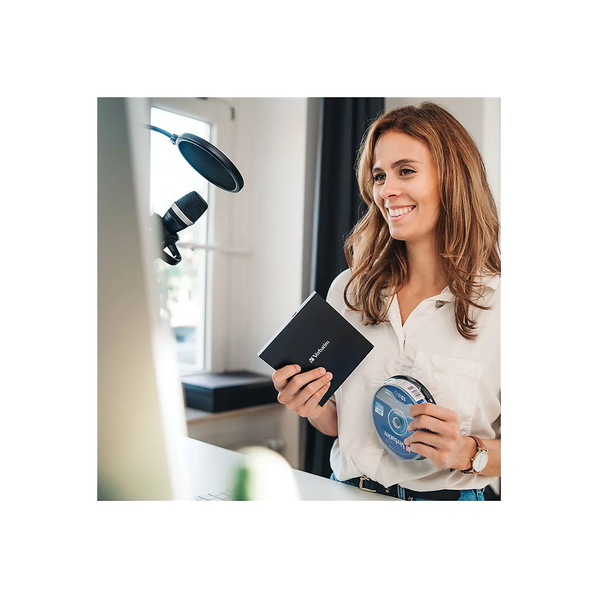 Eine Frau hält lächelnd eine schwarze Festplatte und eine CD in der Hand, Mikrofon im Hintergrund.