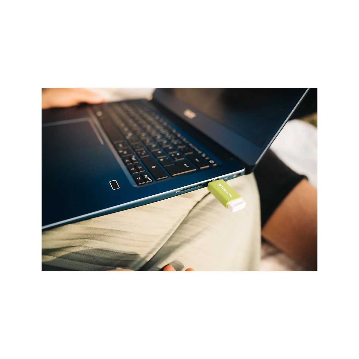 Ein blaues Notebook mit grÃ¼nem USB-Stick. Der Laptop liegt auf einem SchoÃŸ.