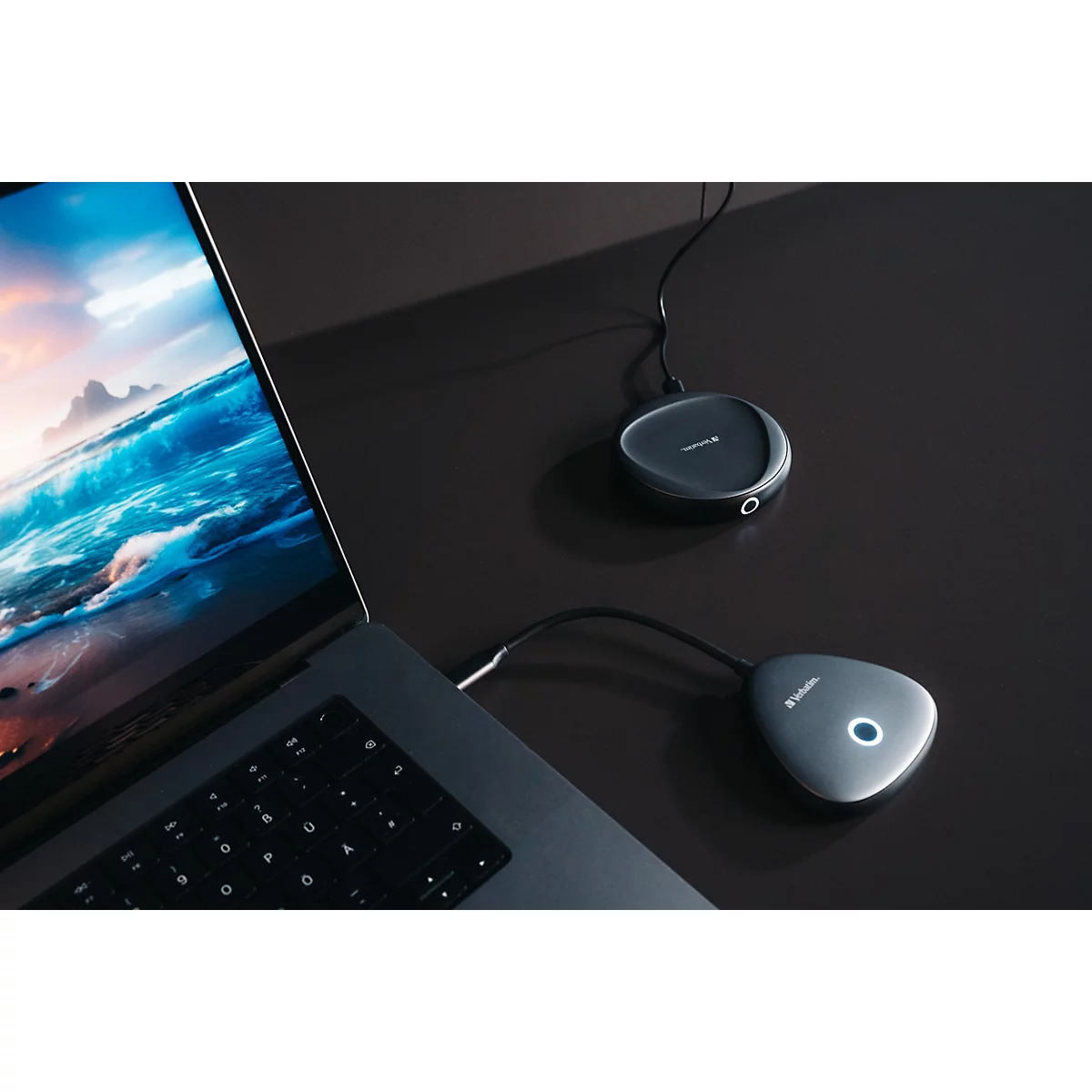 Laptop auf dunklem Schreibtisch mit zwei verbundenen, dreieckigen Konferenz-Hubs, einer leuchtet blau.