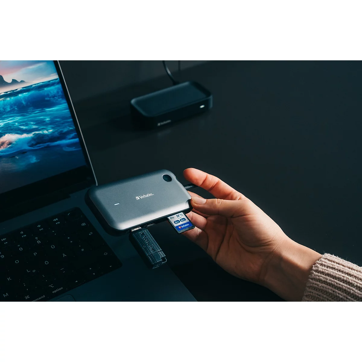 Eine Hand schiebt eine SD-Karte in einen grauen USB-C-Hub, der an einem Laptop angeschlossen ist.