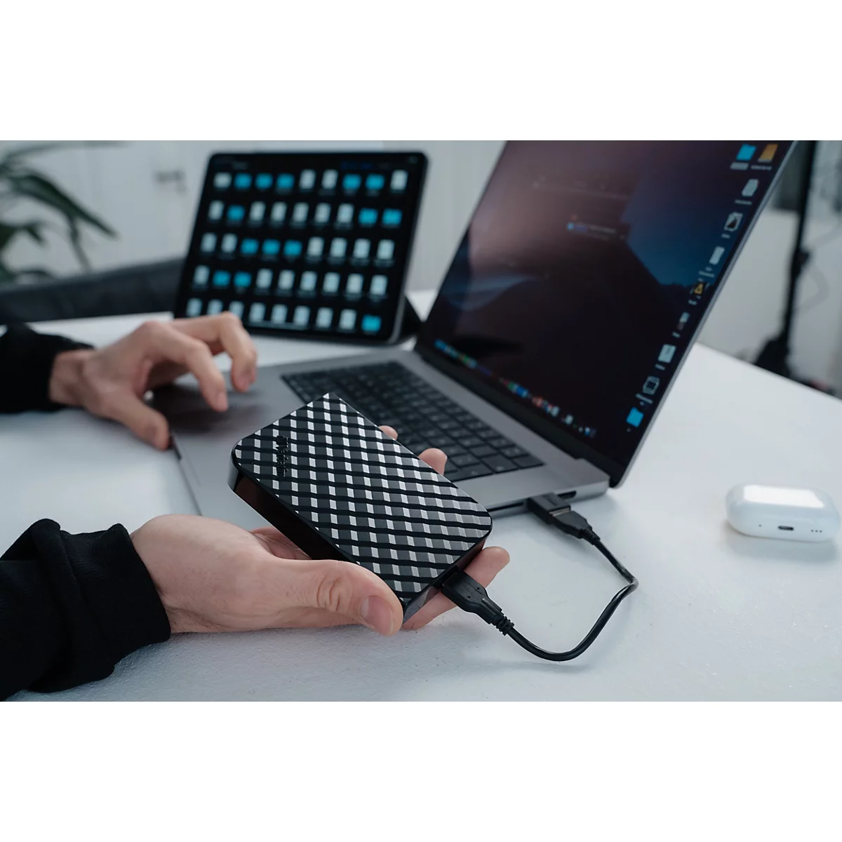 Person hält eine schwarze, gemusterte externe Festplatte, die per USB-Kabel an einen Laptop angeschlossen ist.