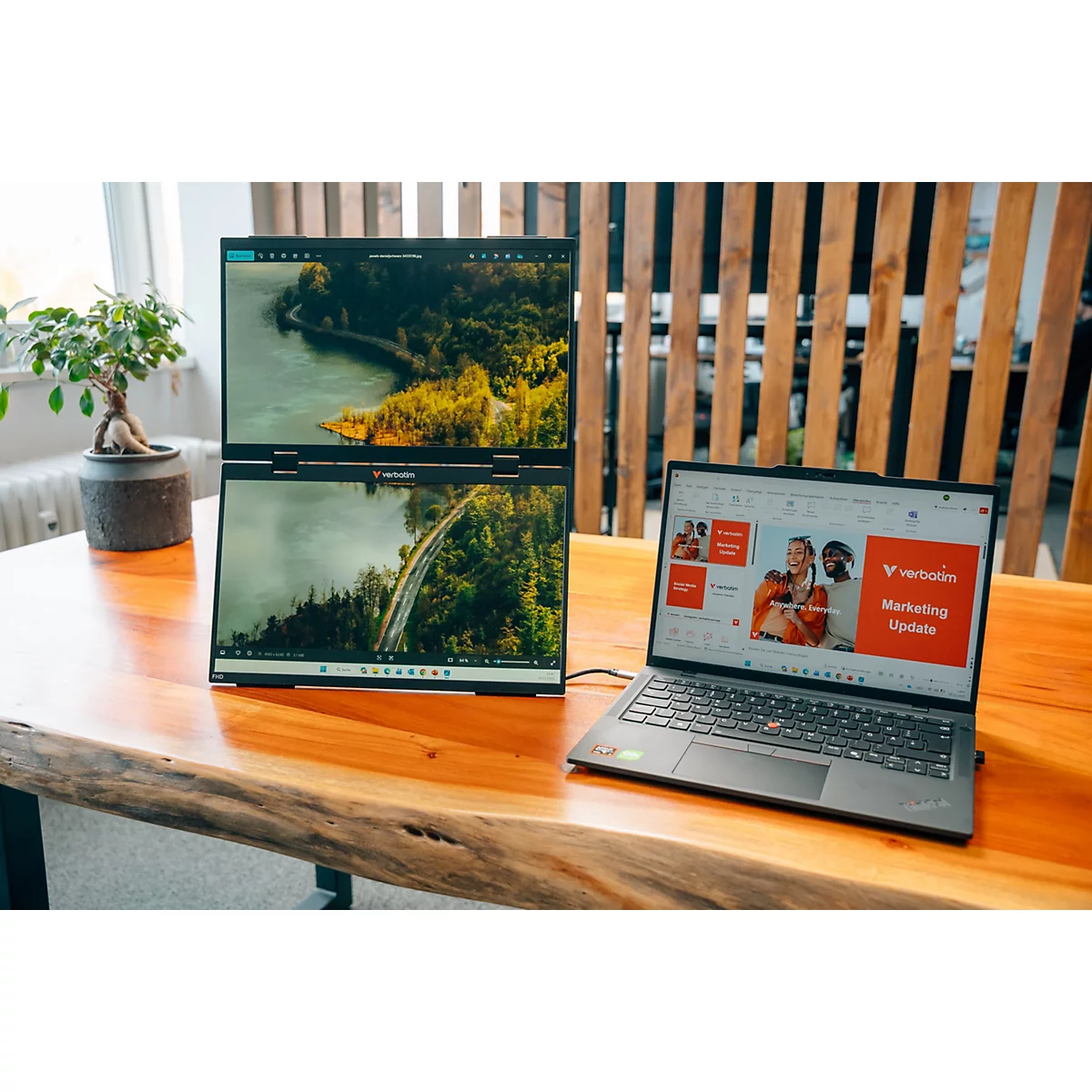 Ein Laptop mit einem vertikal gestapelten Dual-Monitor-System steht auf einem Holztisch in einem modernen Büro.