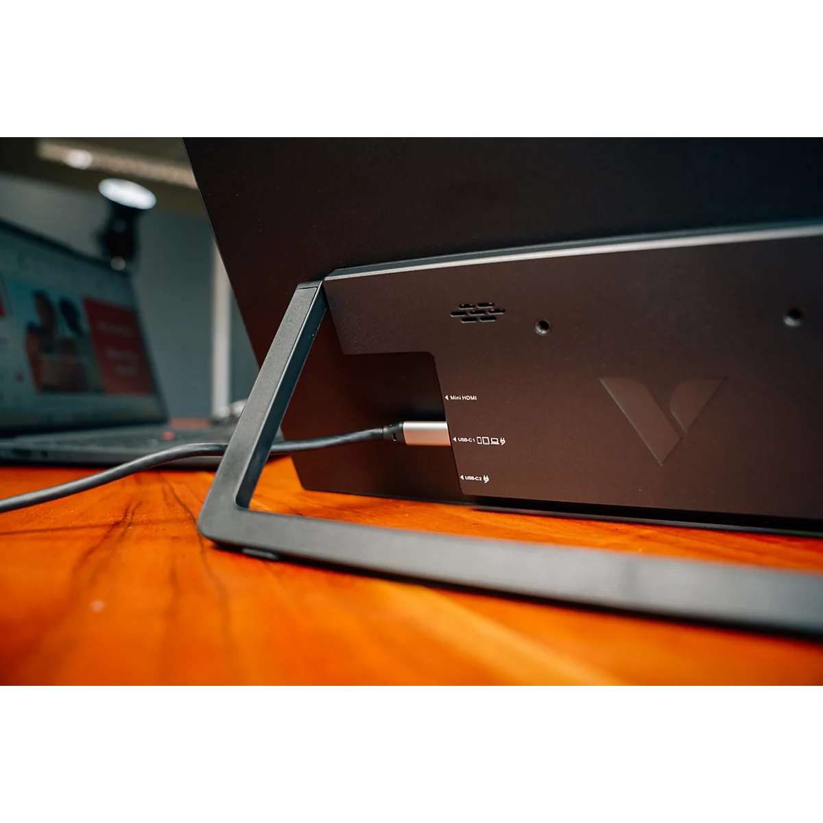 Rückseite eines Monitors mit Standfuß und USB-C-Anschluss auf einem Holztisch.