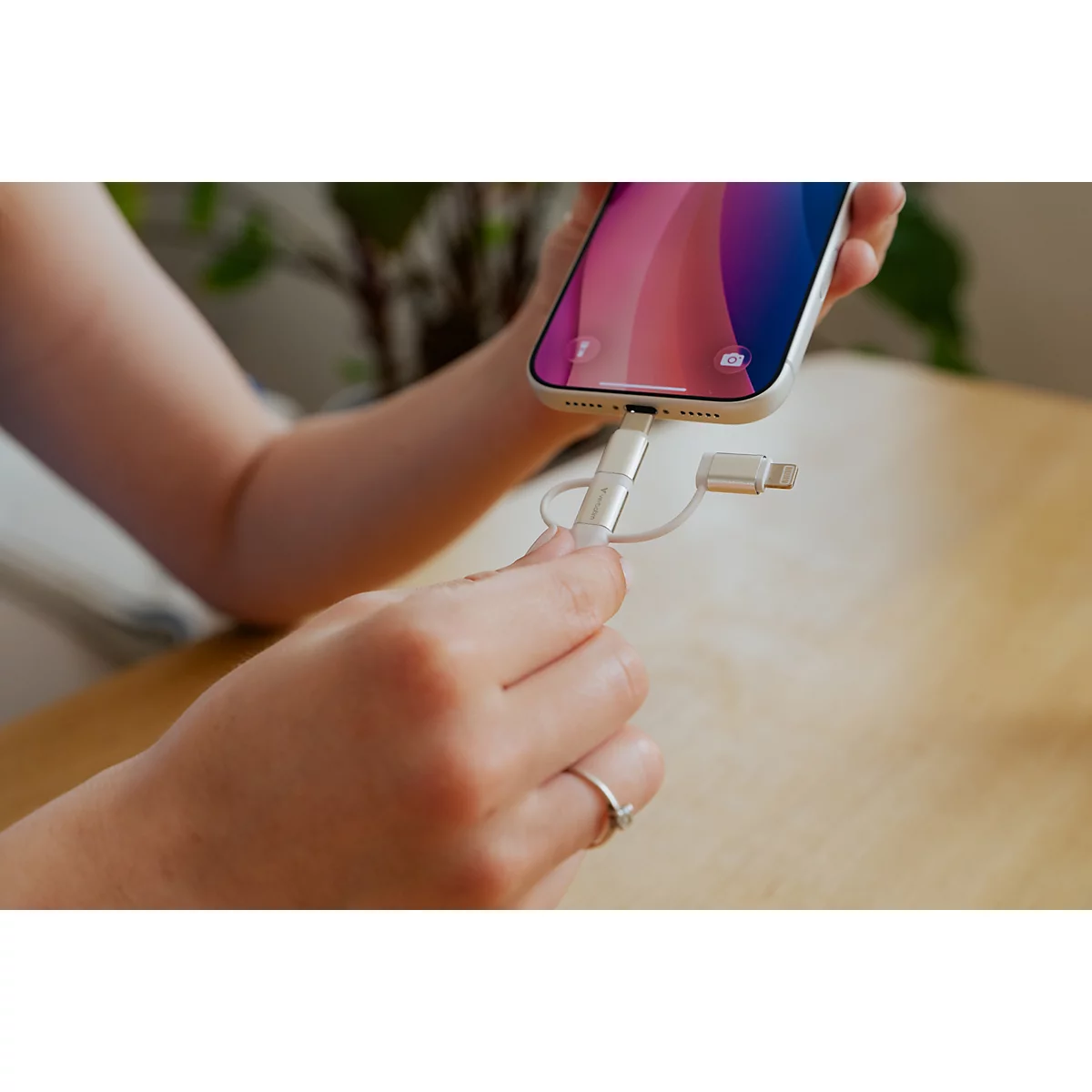 Person steckt einen weißen Ladeadapter in den Anschluss eines hellen Smartphones.