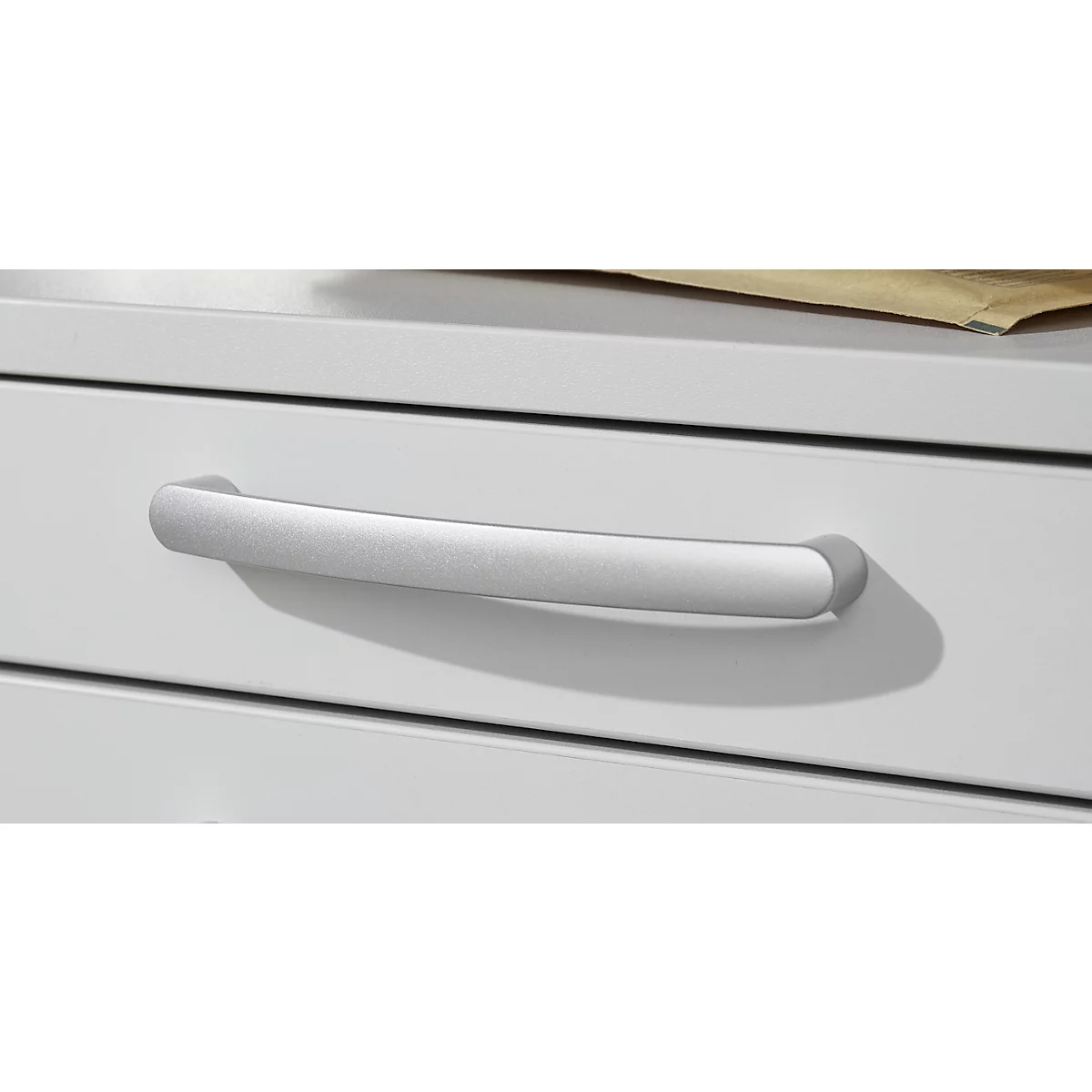 Zilveren handgreep op een witte lade die een schaduw werpt.