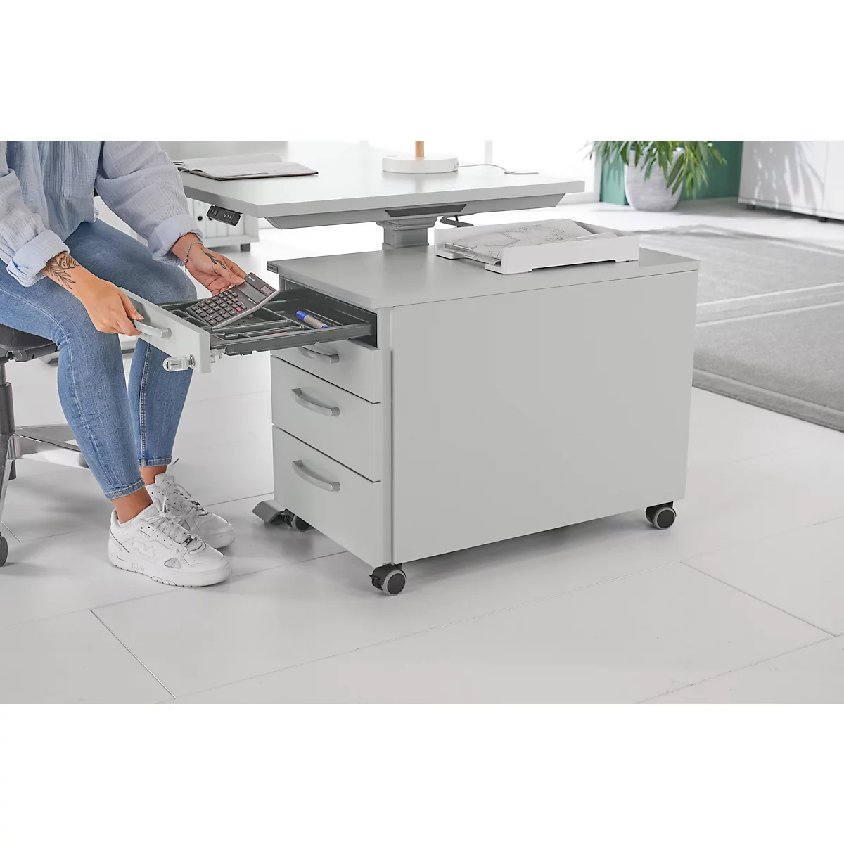 Persoon opent een lade van een rolcontainer. Pennen en een toetsenbord liggen in de container.