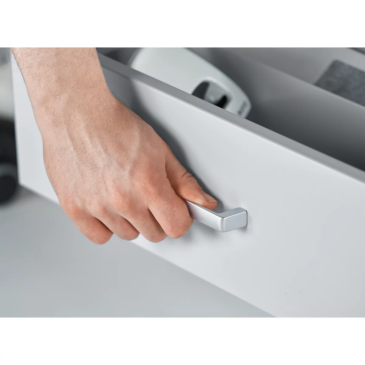 Een hand opent een grijze lade aan een zilveren handvat. Binnenin zijn nog meer grijze objecten zichtbaar.