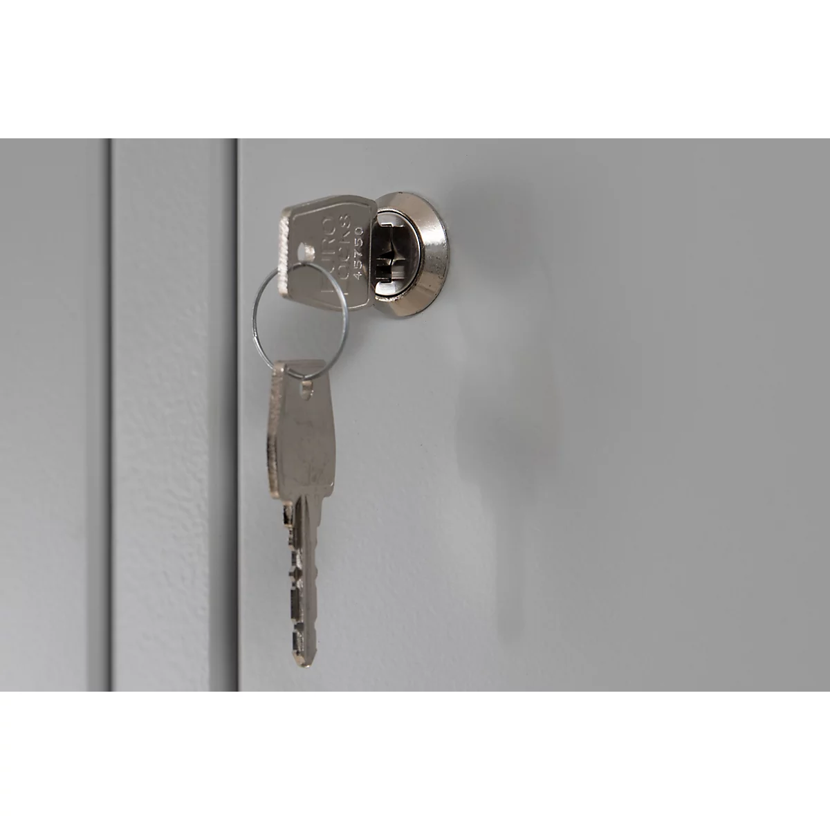 Une clé insérée dans la serrure d'une porte d'armoire métallique grise.