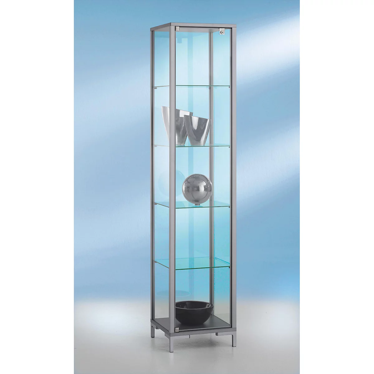 Vitrine étroite avec étagères en verre, remplie d'objets décoratifs. Socle anthracite et cadres argentés.