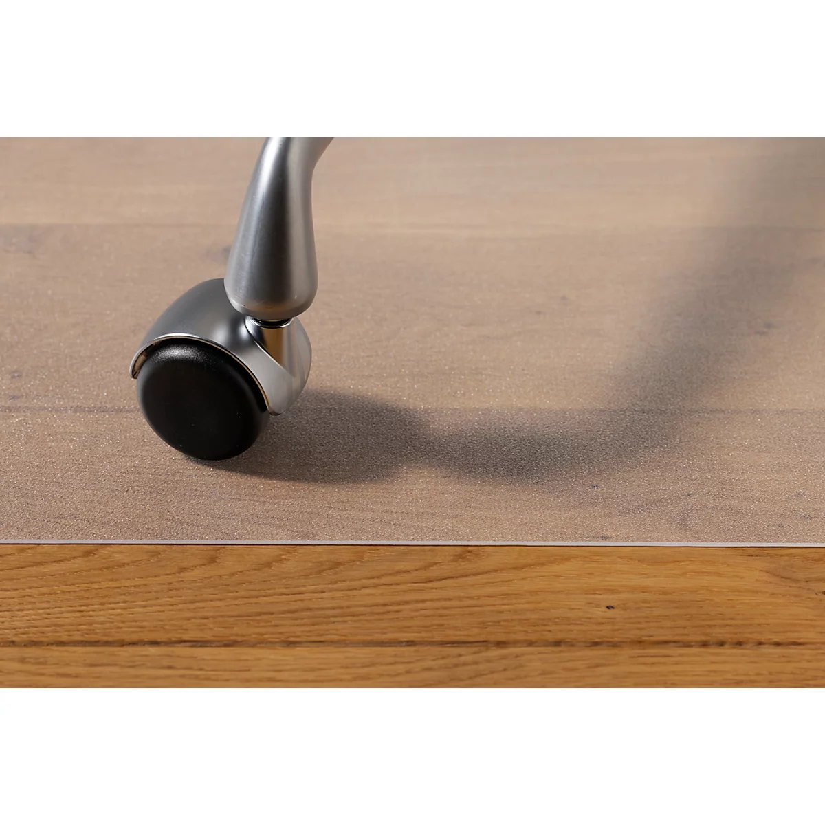 Close-up van een stoelpot op een houten vloer. De zwarte kunststof zwenkwiel en de metalen poot werpen schaduwen.