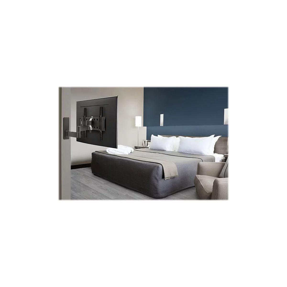 Ein Fernseher hängt an einer Halterung über einem Bett. Das Zimmer ist modern eingerichtet, mit Sofa und Nachttisch.