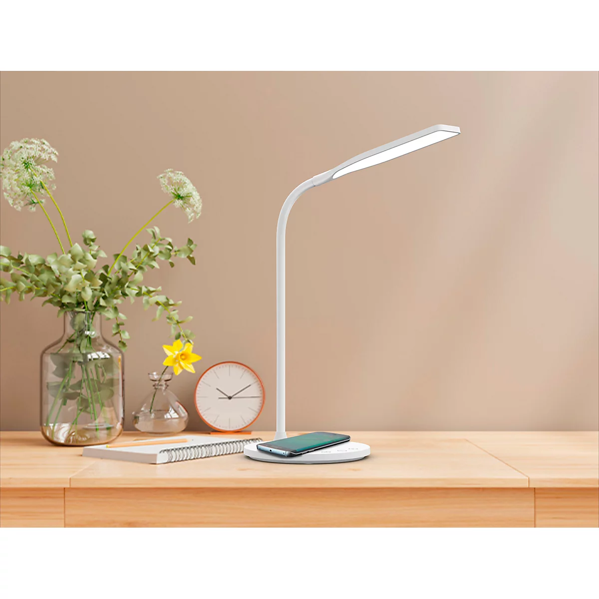 Bureau met lamp, telefoon en bloemen. De witte lamp brandt. Op het bureau liggen een telefoon, een klok en een notitieblok.