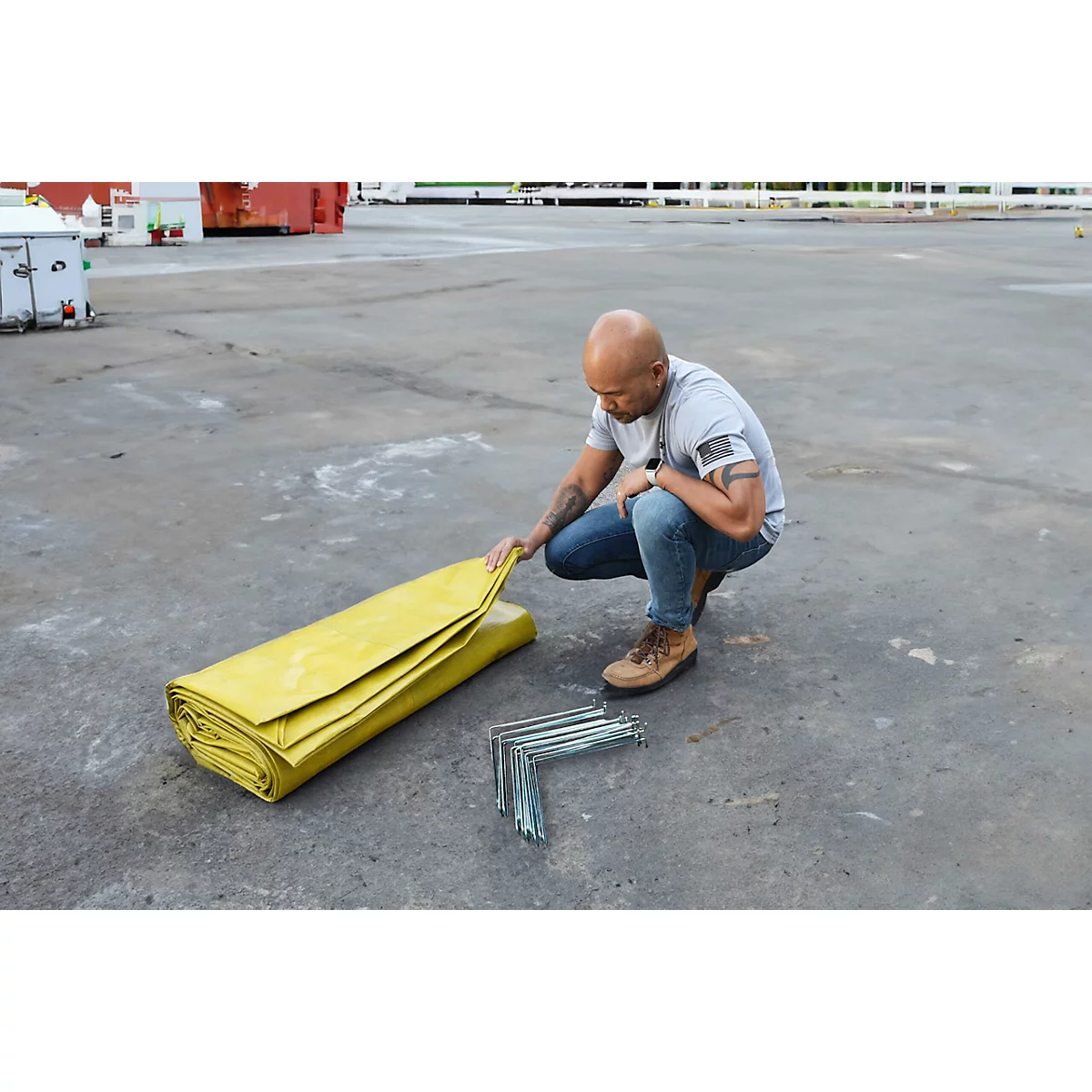 Een man knielt naast een gele gevouwen zeildoek. Naast hem liggen hoeken en hij raakt het zeildoek aan.