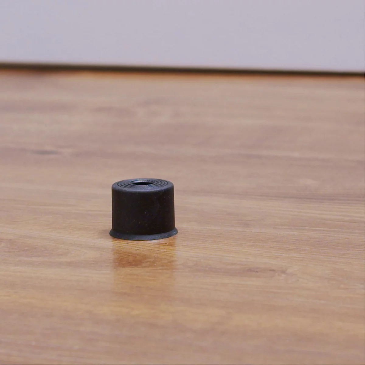 Schwarzer Zylinder auf Holz. Der Zylinder hat eine runde Öffnung in der Mitte.