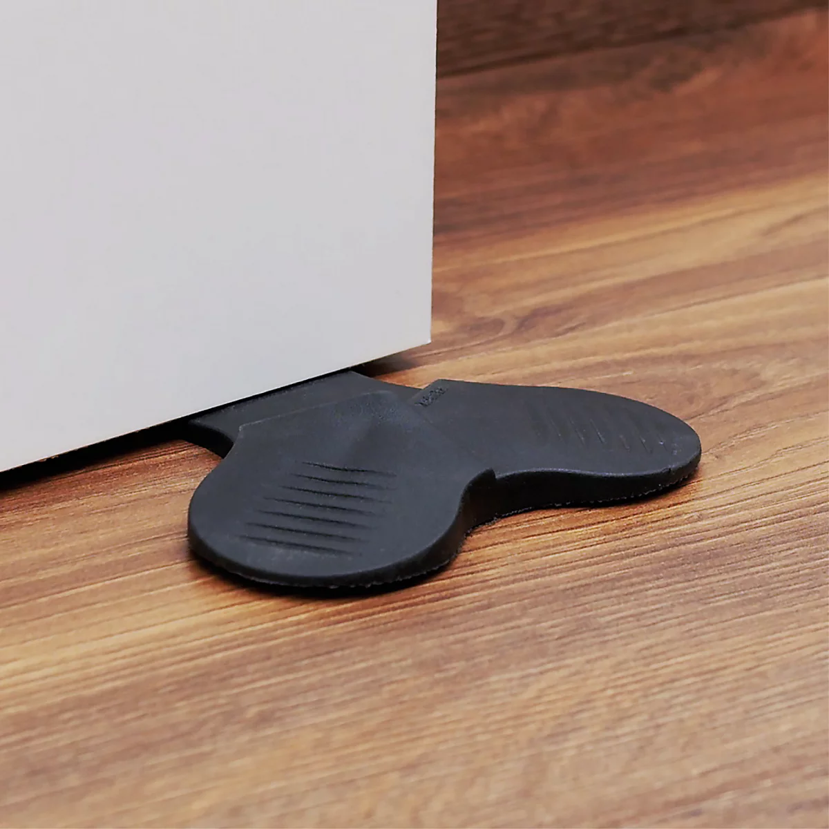 Zwarte rubberen deurstoppers voor een witte deur op een houten vloer.