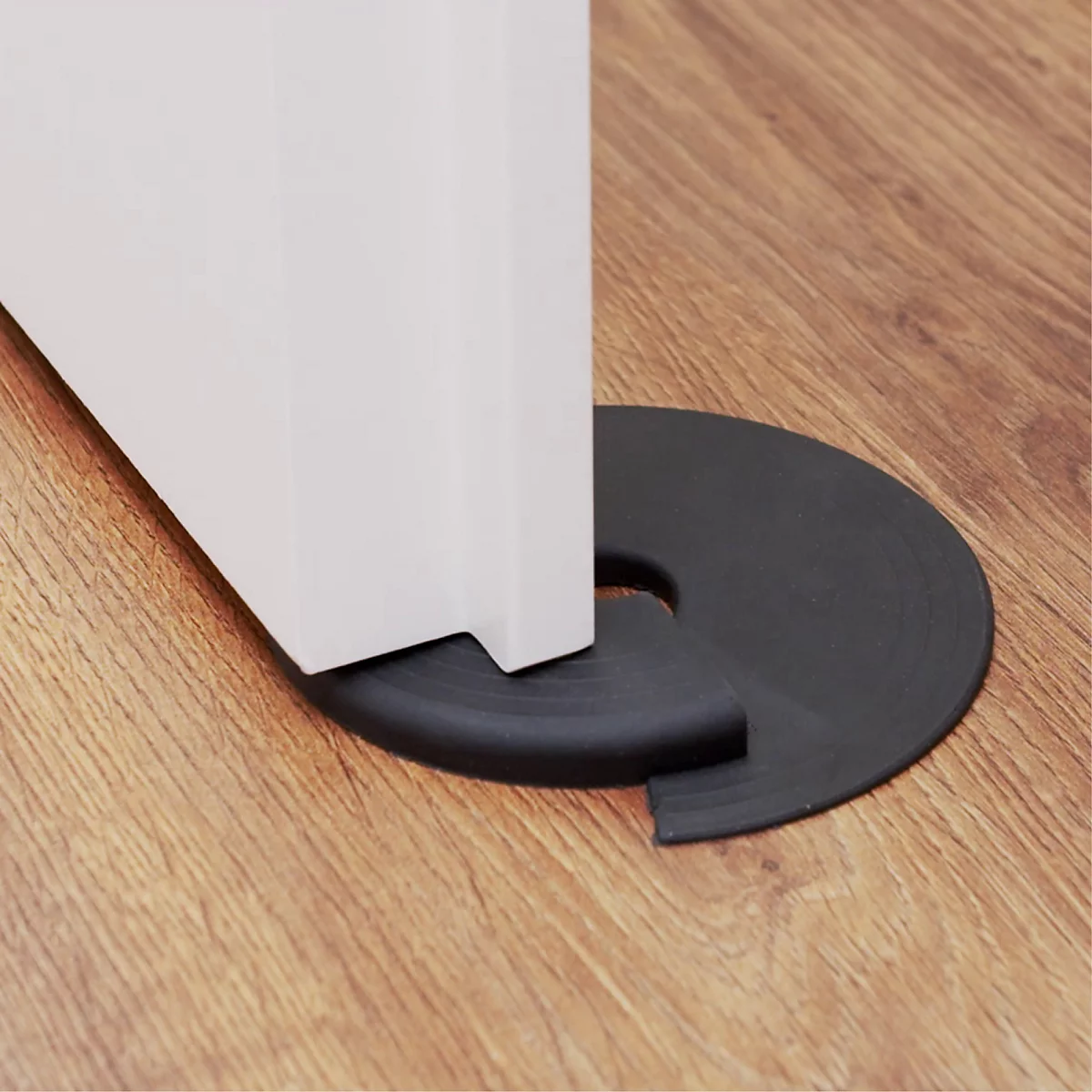 Zwarte rubberen deurstopper onder een witte deur op houten vloer.