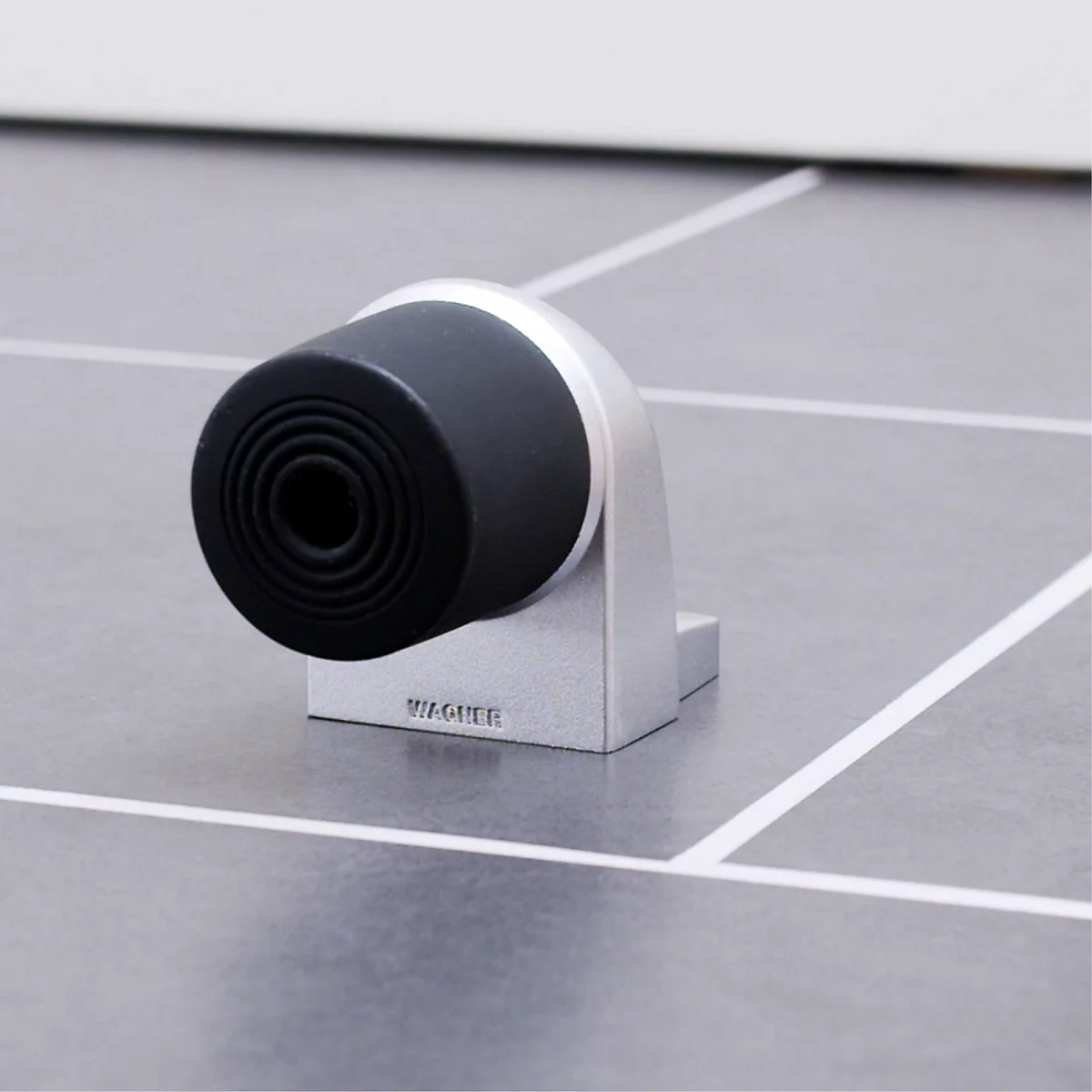 Close-up van een deurbuffer gemaakt van metaal en rubber. Het zwarte rubberen deel is gemonteerd op een metalen houder, het oppervlak is gegraveerd met de tekst "WAGNER".