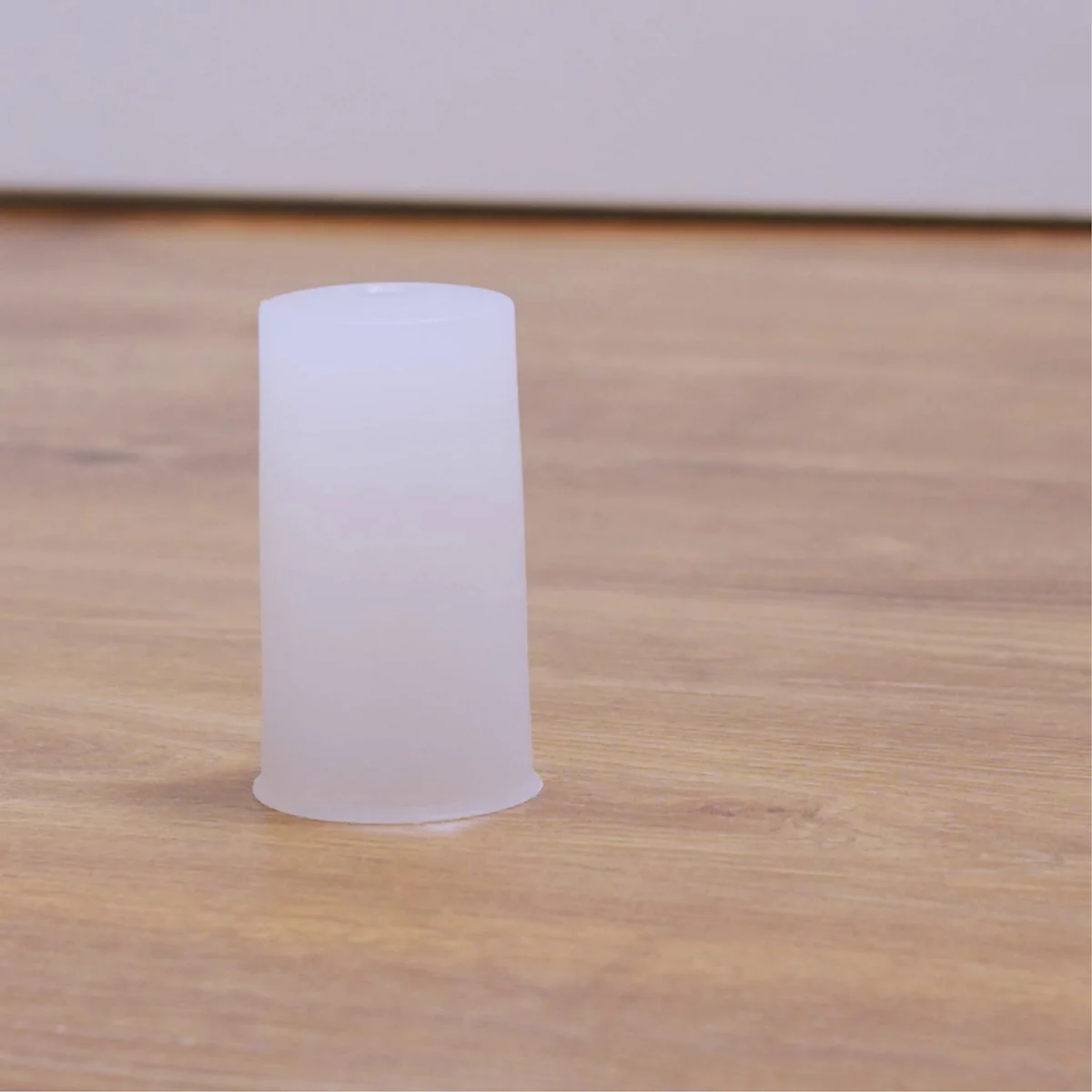 Een transparante, kegelvormige plastic beker staat op een houten vloer. De beker heeft een bredere opening en loopt taps toe naar beneden.