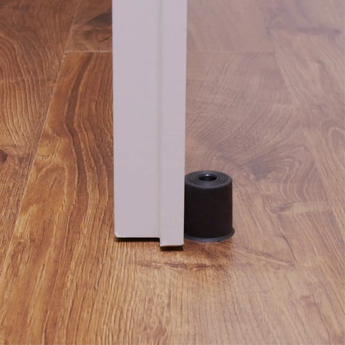 Zwarte deurstopper die een deur op een houten vloer vastzet.