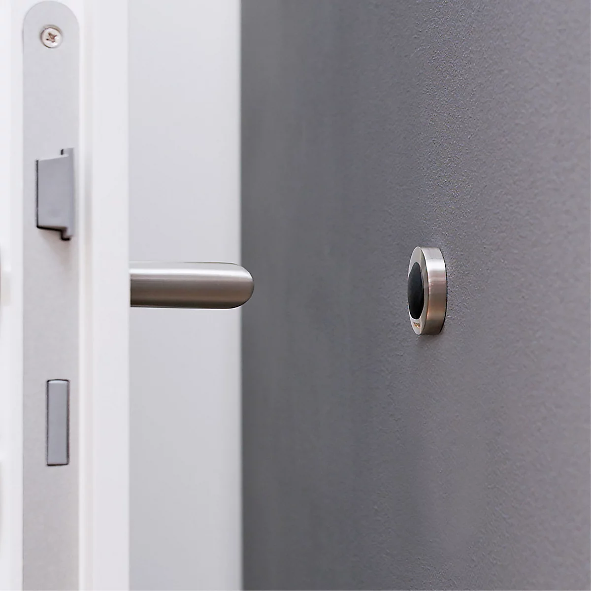 Detailopname van een witte deur met roestvrijstalen handgreep en een deuropener met donkere binnenkant op een grijze muur.
