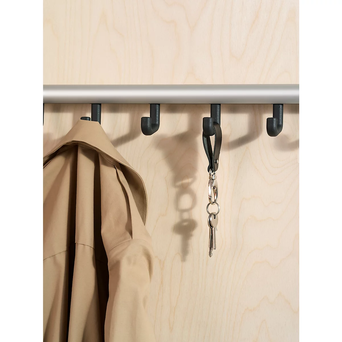 An einer Garderobenleiste hängen Jacke und Schlüssel. Die schwarze Garderobenleiste ist an einer Holzwand montiert.