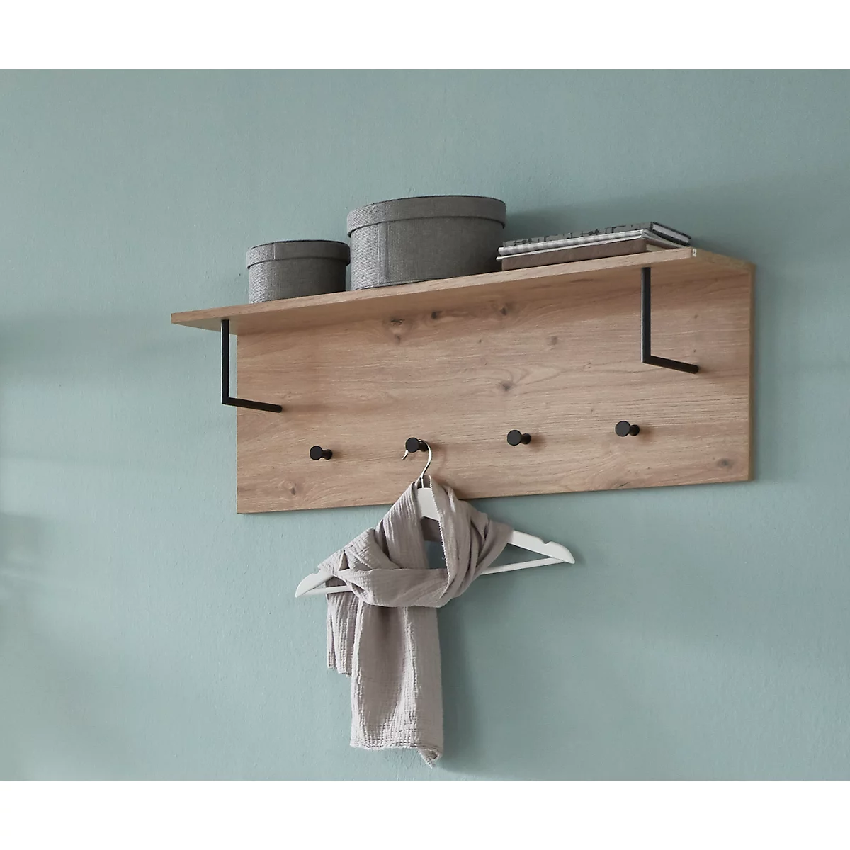 Holzgarderobe mit Hutablage an blauer Wand. Grauer Schal hängt an einem Haken.