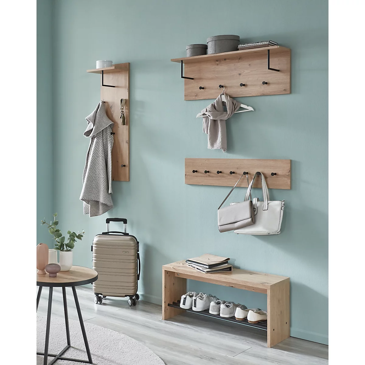 Ein Flur mit Garderobe, Gepäck und Schuhen. Helle Holzmöbel an blauer Wand. Handtuch, Schal und Taschen hängen. Rollkoffer, Schuhe auf Bank.